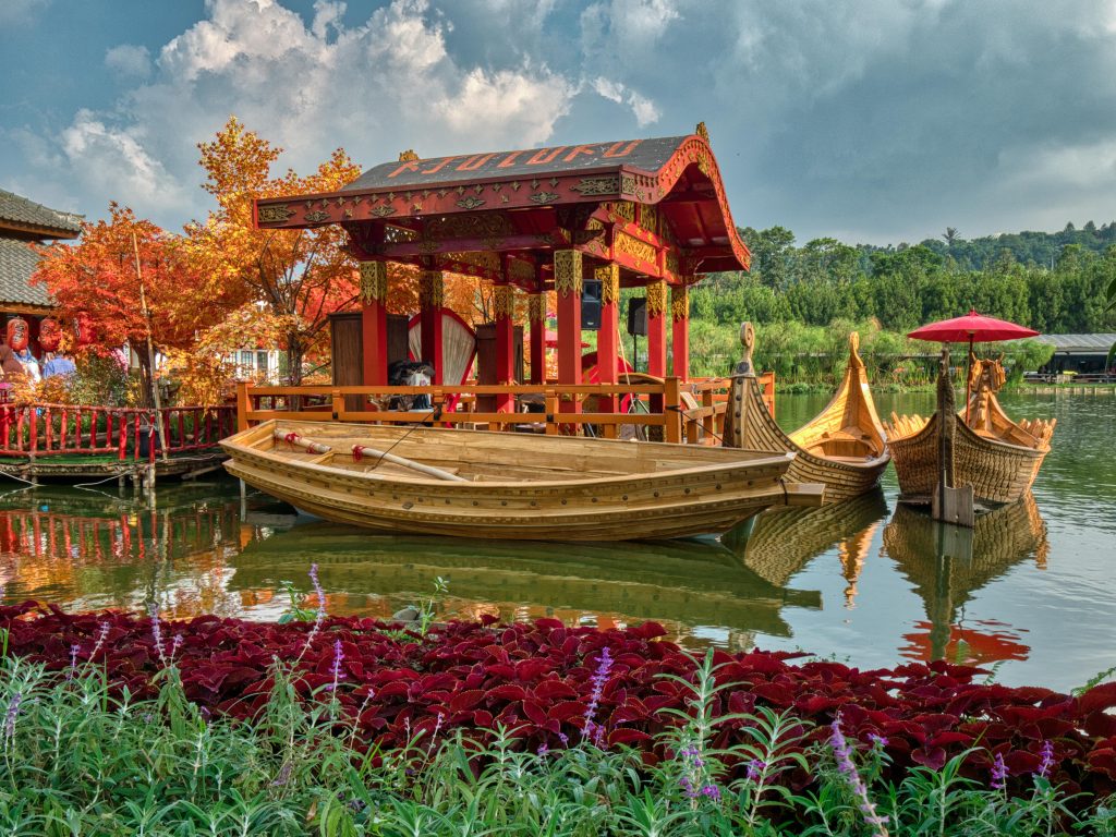 Vibrant Japanese-styled boats on a tranquil lake in Bandung, surrounded by lush greenery and colorful flowers.