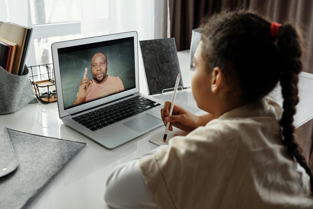 A child engaged in online learning with a teacher on a laptop during a virtual session indoors.